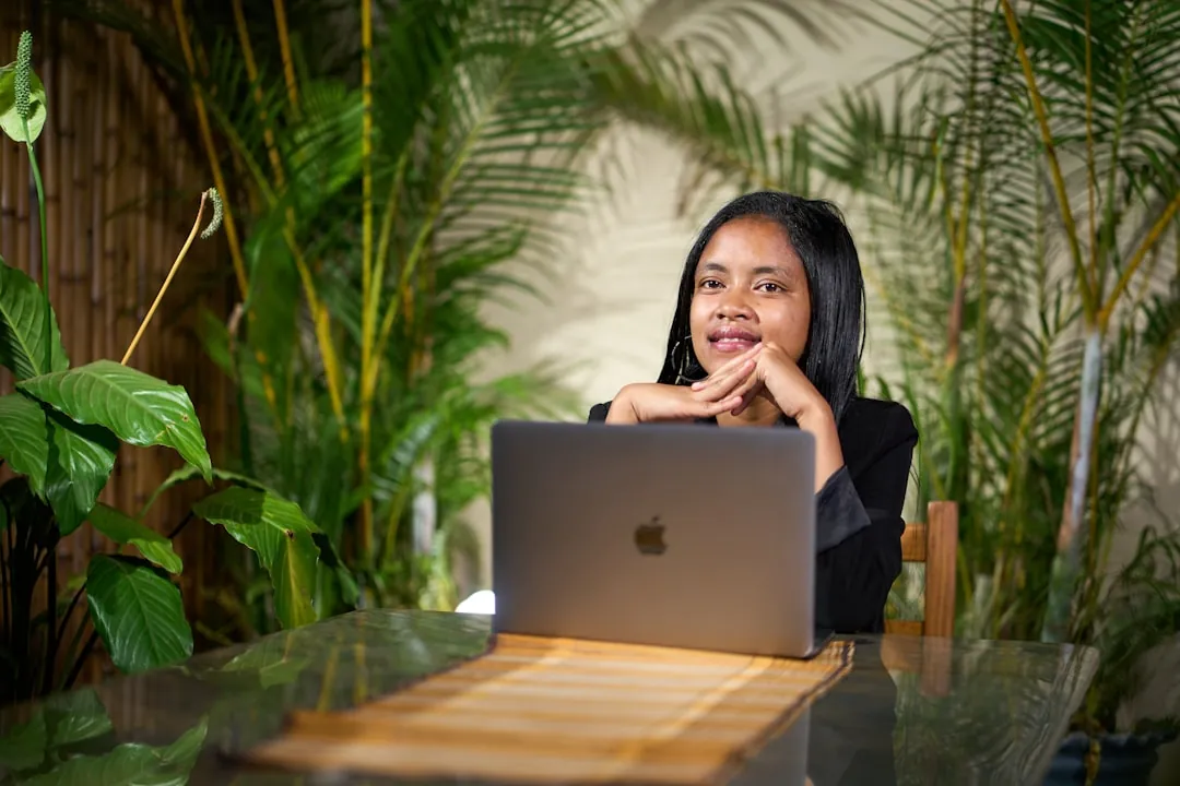 Young woman working on a laptop surrounded by plants.